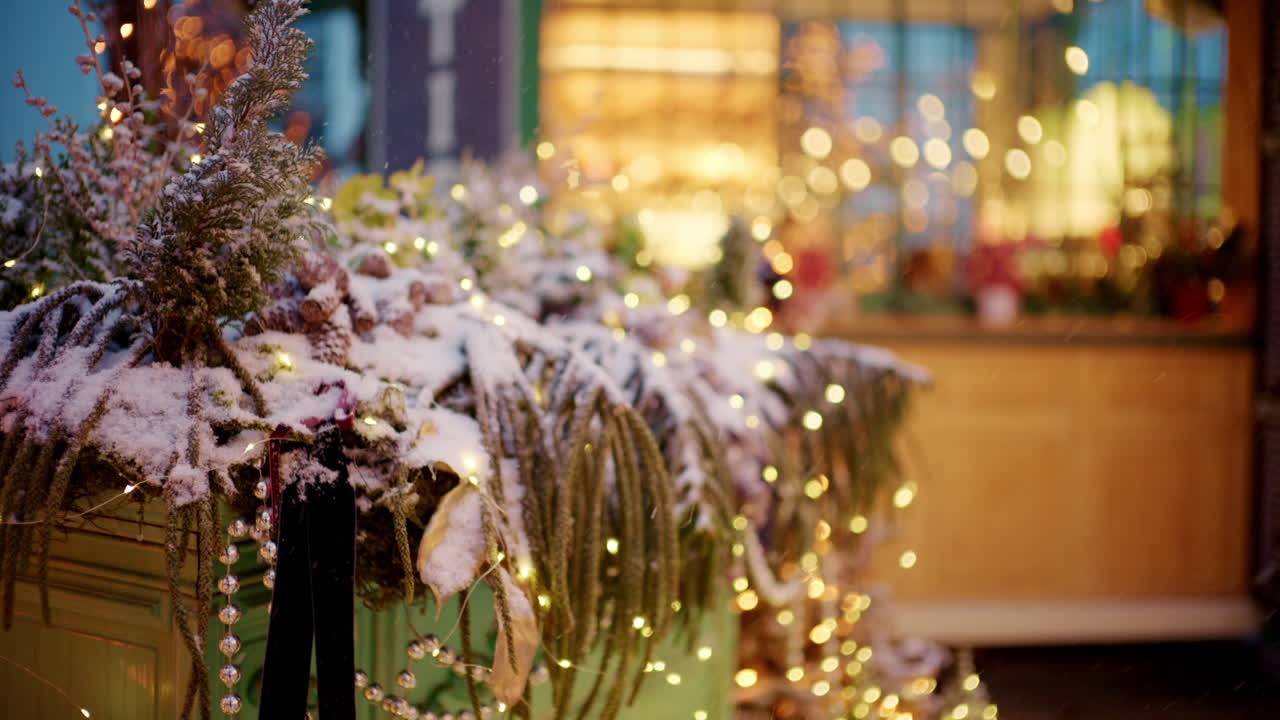 Close-up van een decoratieve plantenbak gevuld met wintergroen, bedekt met sneeuw en omwikkeld met kleine gloeiende lichtjes.