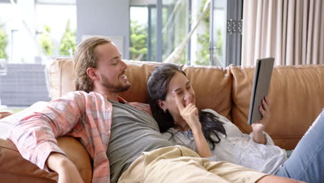 a young diverse couple relaxes on a sofa at home, using a tablet