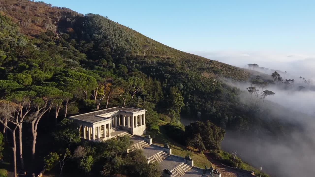 Rhodes Memorial with statues University of Cape Town Upper Campus below Devils Peak. Low pressure weather creating low hanging clouds brought from a North Western wind. Aerial shot towards Pine trees