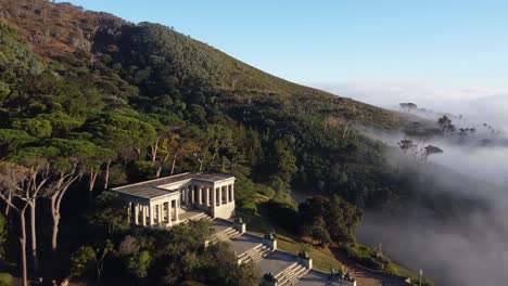 rhodes memorial with statues university of cape town upper campus below devils peak. low pressure weather creating low hanging clouds brought from a north western wind. aerial shot towards pine trees