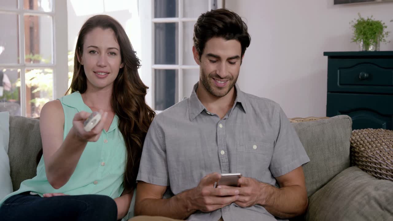 pareja linda viendo televisión y usando el control remoto en el sofá