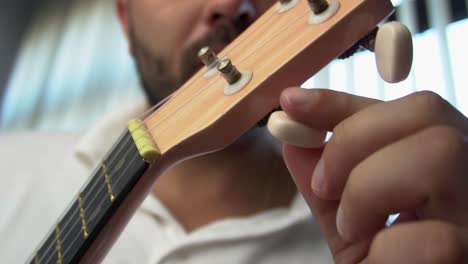hombre de mediana edad 30 y con cuentas está jugando y silbando con su ukulele rosado al lado de una gran ventana y cerca de una planta verde