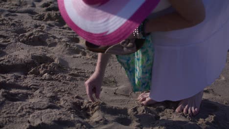 Middle-aged-white-woman-picking-up-rocks-in-Venice-Beach,-California-in-slow-motion