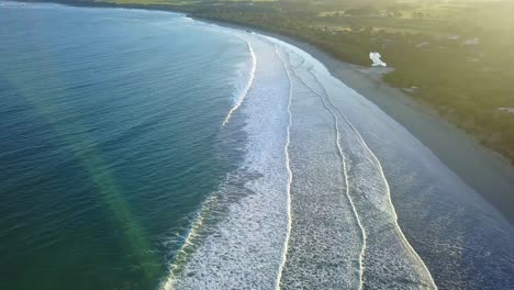 foreard moving aerial footage into the sun of waves hitting beach at inverloch, victoria, australia