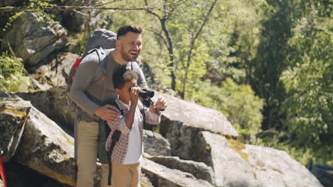 happy father and son looking through binocular during hike