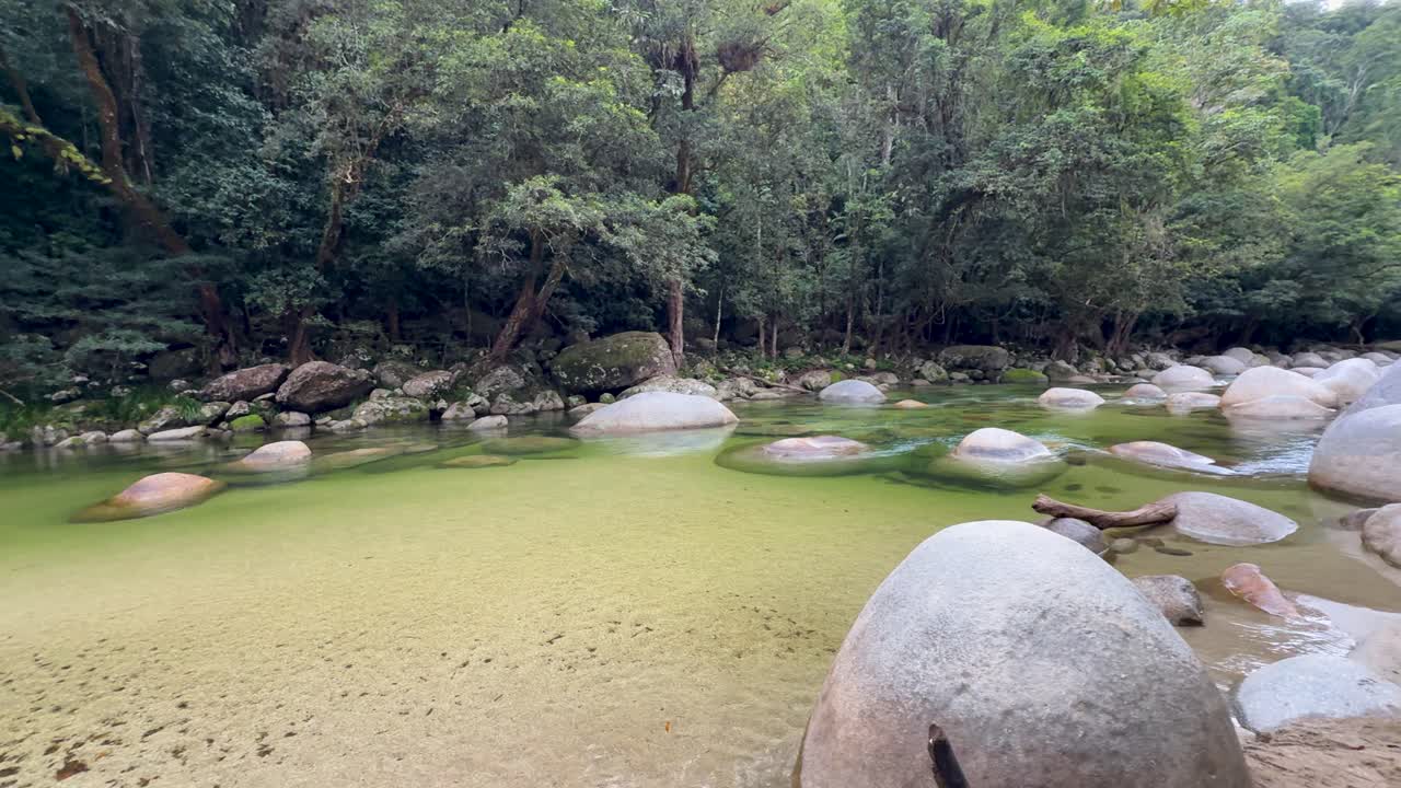 Calm river with large boulders and lush rainforest. Soft lighting creates a serene atmosphere in Port Douglas, Queensland