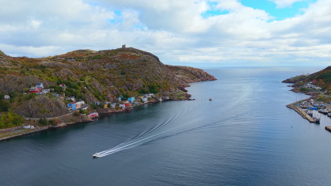 A sweeping aerial view over Fort Amherst follows a winding waterway between steep hills, vibrant fall foliage and rocky outcrops leading to the bay under a clear sky