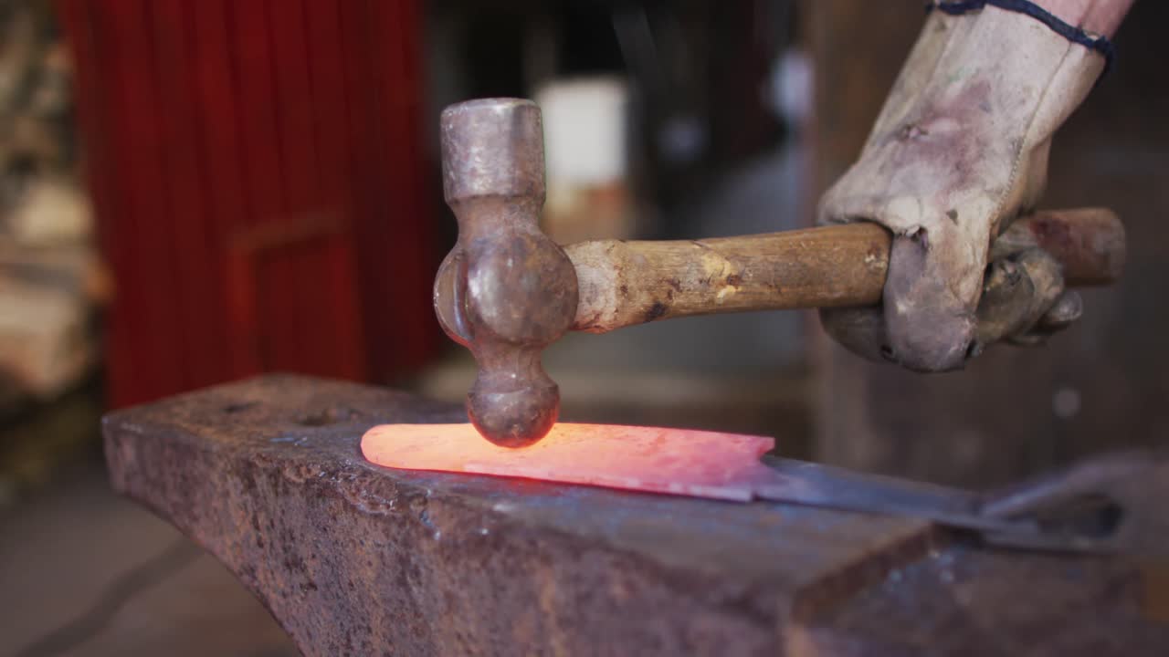 manos cercanas de un hombre caucásico fabricante de cuchillos en un taller sosteniendo un martillo y haciendo un cuchillo
