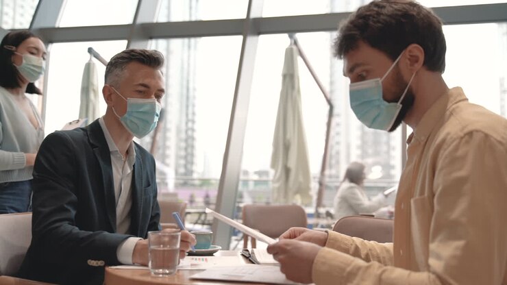 Un team di lavoro con mascherine si scambia saluti col gomito in un bar.