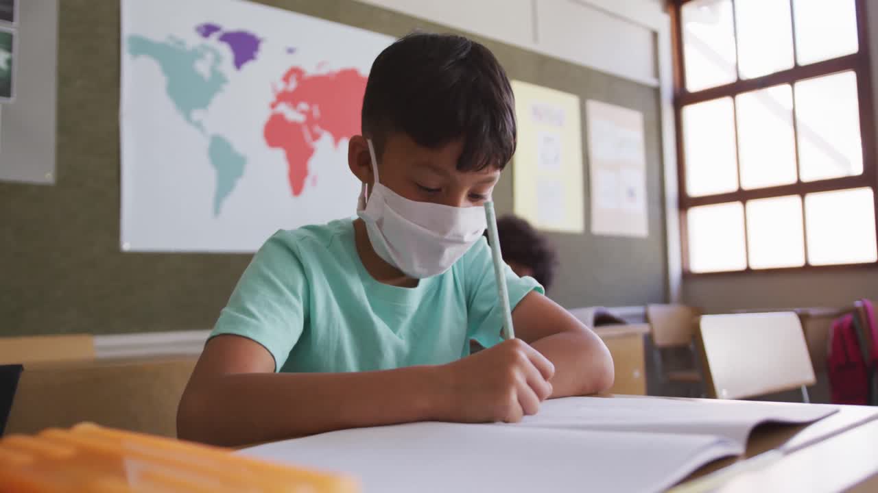 학교 의 책상 에 앉아 있는 소년 이 얼굴 마스크 를 쓰고 재채기 하고 있다
