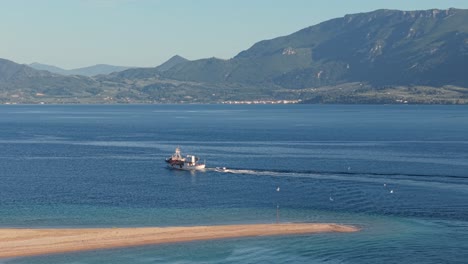 a fishing trawler navigates out from the narrow artemisium strait into the open waters of north evoikos gulf, surrounded by rugged coastline and calm sea