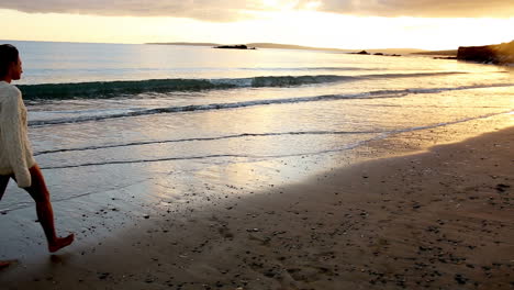 Woman-walking-along-the-water-at-sunset