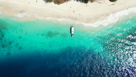 Top-view-of-traditional-boat-anchoring-on-shoreline-of-tropical-island-with-white-sandy-beach-washed-by-blue-azure-sea-waves,-Indonesia