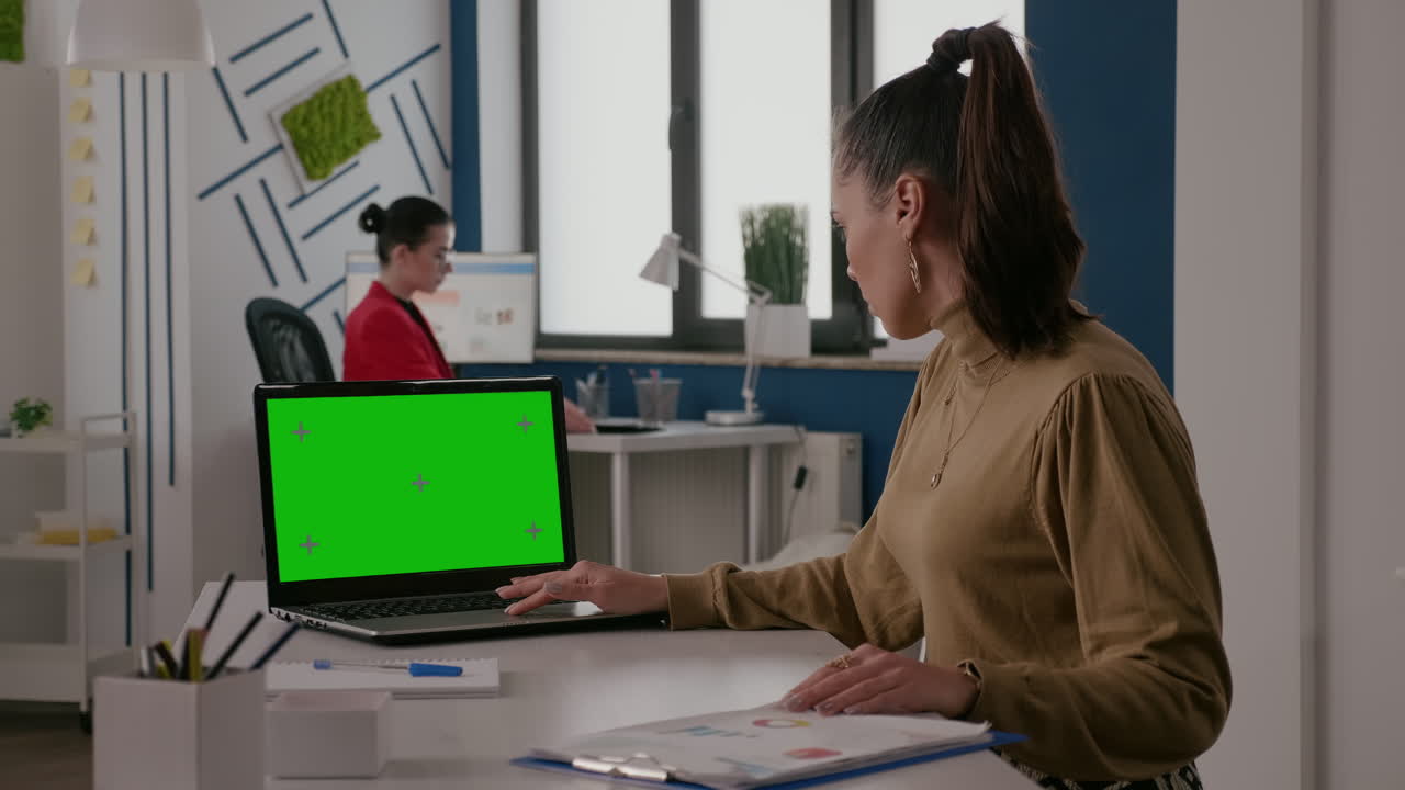 Woman sitting at desk with green screen on laptop