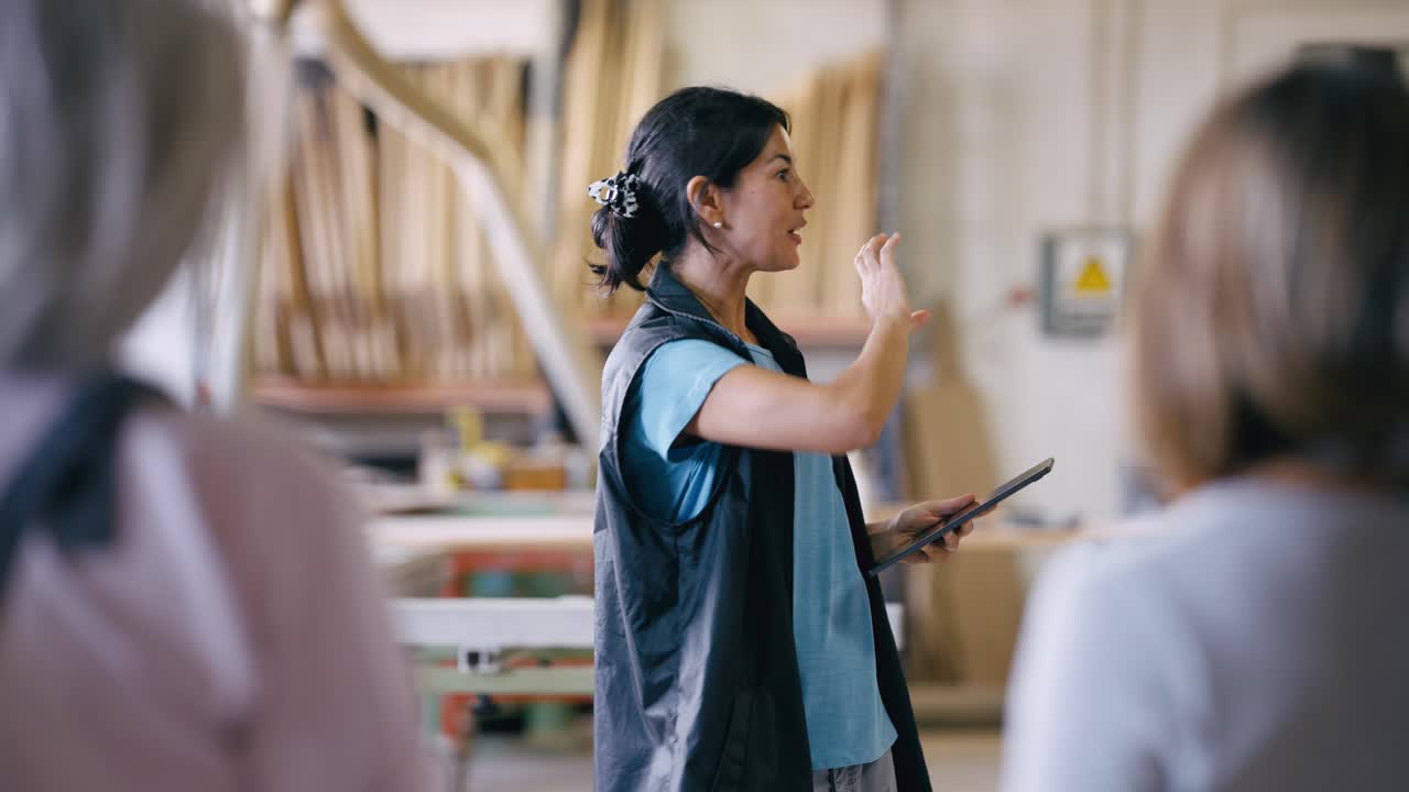 Female Manager Explaining to Employees in a Workshop with a Tablet