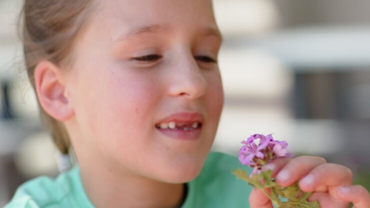 Un bambino che tiene lo stelo, porta dei fiori rosa al naso, li annusa e ne ispeziona i petali sul balcone.