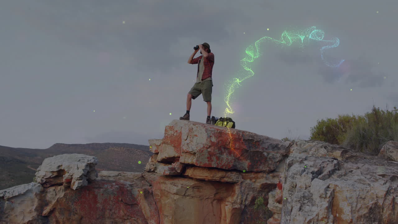 Man scanning hills with binoculars from outcrop, presenting animated map overlay for education