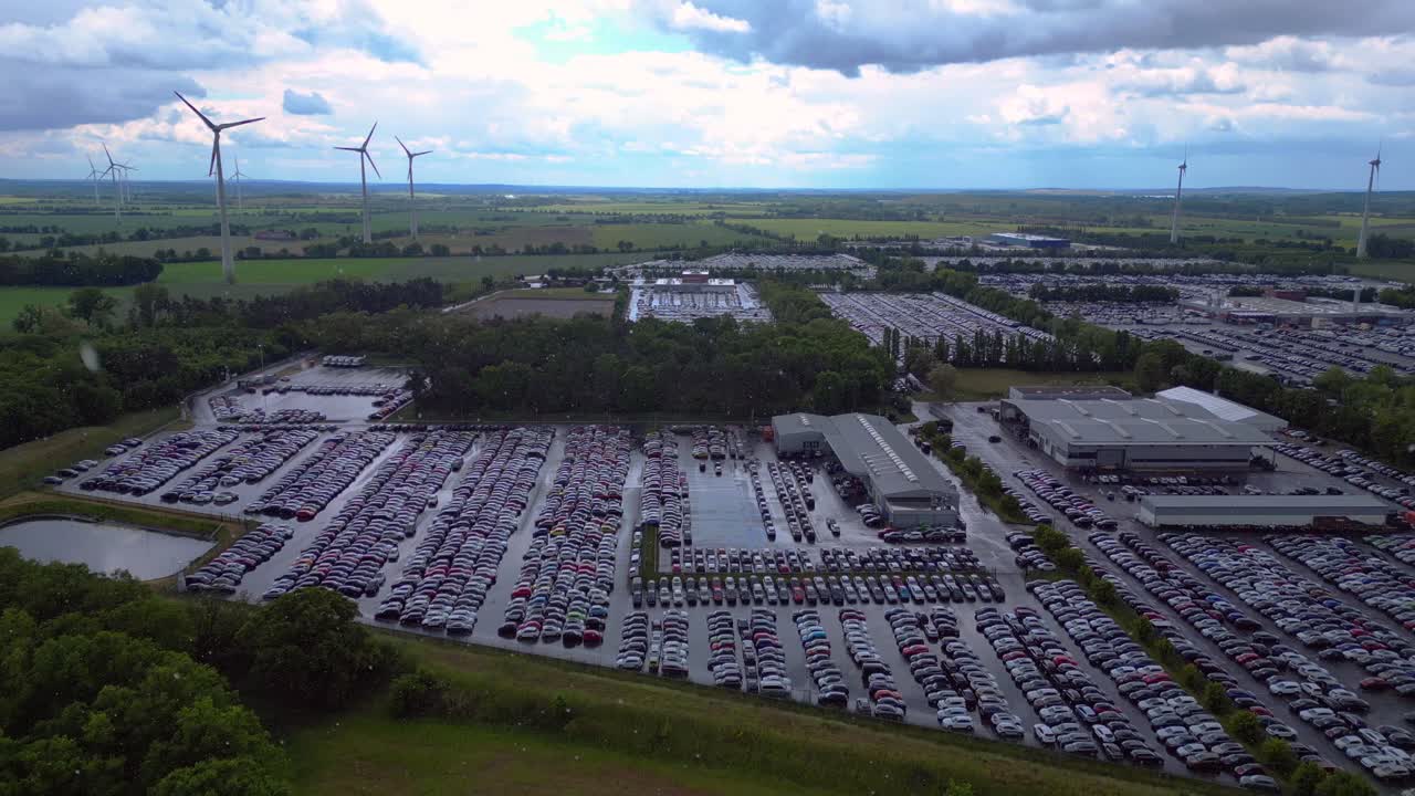 large parking lot full of cars near a wind farm and countryside in Germany. Tremendous raining aerial view flight