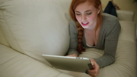 Beautiful-cheerful-brunette-lying-on-couch-using-tablet