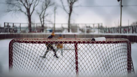 zwei kleine kanadische kinder in winterkleidung spielen hockey auf einer outdoor-hockeybahn in einer kleinen ländlichen gemeinde