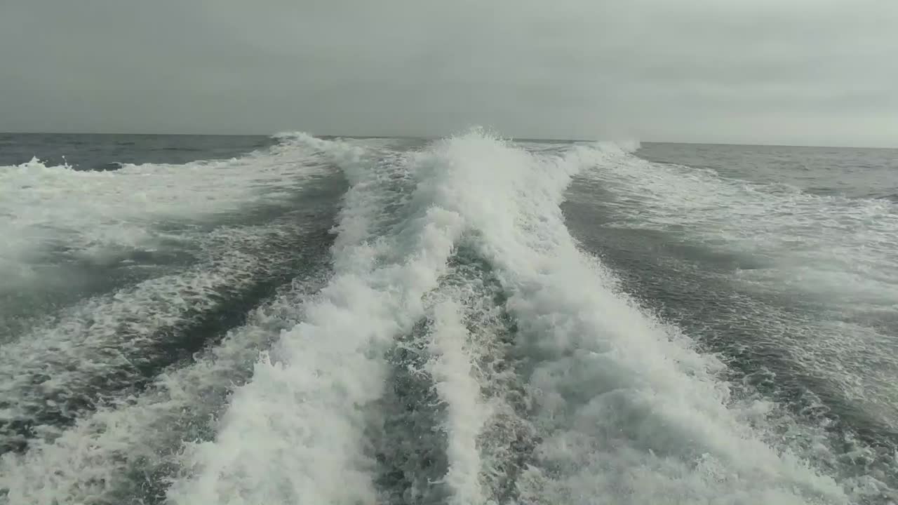 estela de agua vista desde atrás de un bote de motor en movimiento rápido en un día de cielo despejado, mar azul, superficie de agua