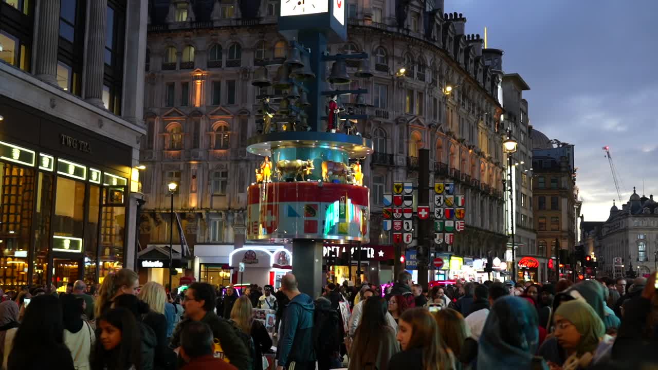 Tourists gather around Leicester Square clock with animated figures in London evening lights