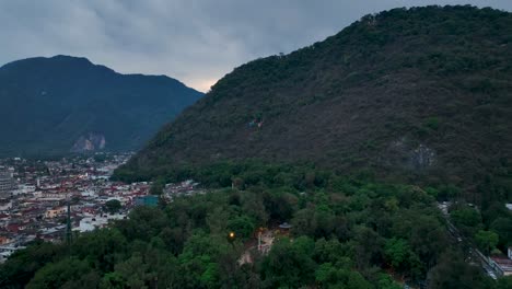 Forward drone move tracks toward the colorful Orizaba Cable Car cabins as they glide over downtown, exposing Cerro del Borrego and a moody overcast sky.