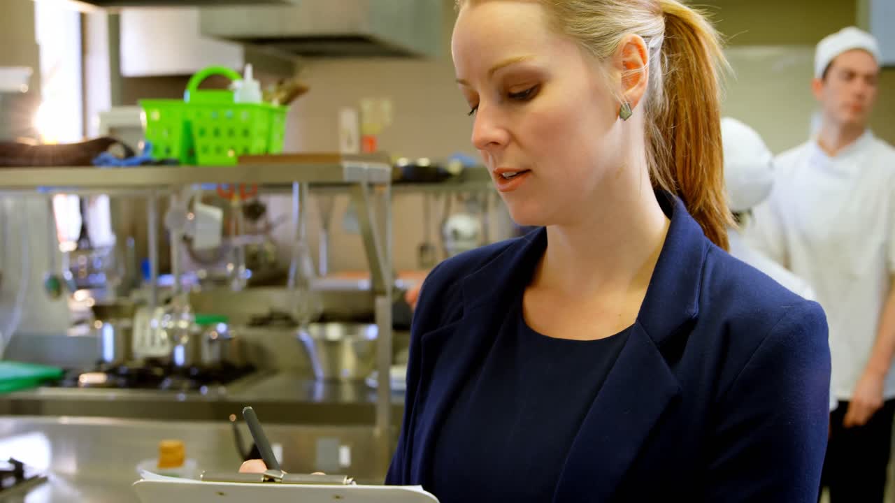 Female manager writing on clipboard in kitchen 4k