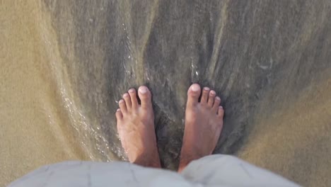 Feet-with-sea-wave-in-slow-motion,-feet-on-the-sand,-top-down-view