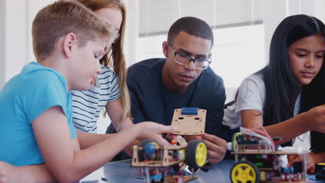 students with male teacher in after school computer coding class learning to build robot vehicle