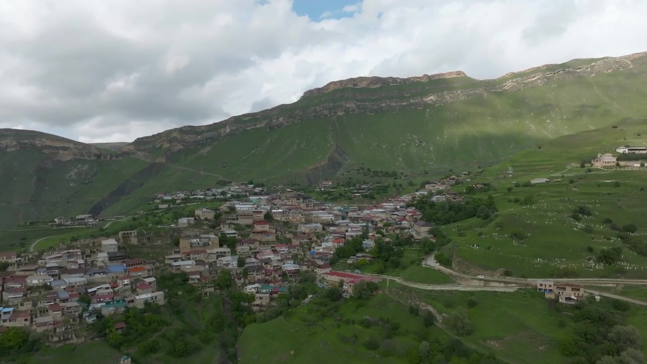 Filmato drone del villaggio di Chokh su verdi pendii montani con fitte case addossate, strada tortuosa e nuvole spettacolari, paesaggio rurale nel Dagestan, Russia