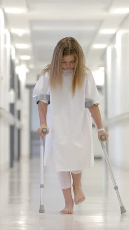 vertical video of caucasian girl patient walking with crutches in hospital corridor, slow motion