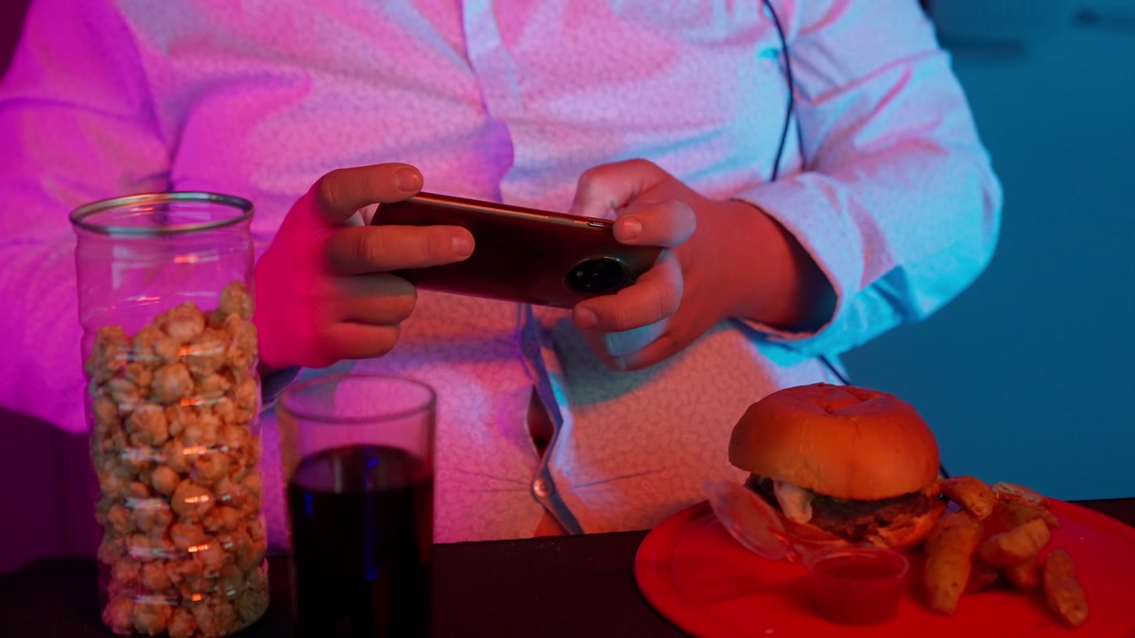 Gamer Playing Mobile Game with Fast Food Under Neon Lights