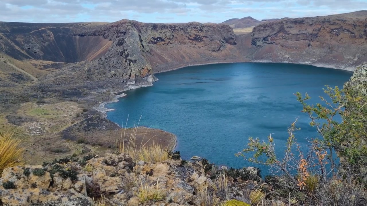 O vento varre as águas azul-profundo da Laguna Azul, um lago de cratera vulcânica no campo vulcânico de Pali Aike na Patagônia, perto de Río Gallegos, Argentina. Paisagem remota deslumbrante moldada por forças vulcânicas