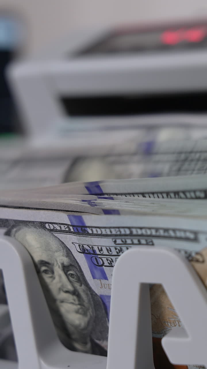 Notes with Benjamin Franklin portraits fall on the holder of cash counting machine. Close up. Blurred background. Vertical video