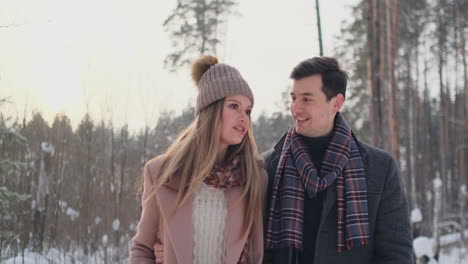 in the winter snowy forest, young men and women dressed in coats and scarves are walking and having fun. loving couple spend together valentines day.