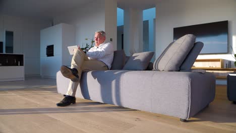 sunset work mode: man engaged in tablet work on sofa, bathed in sunset glow