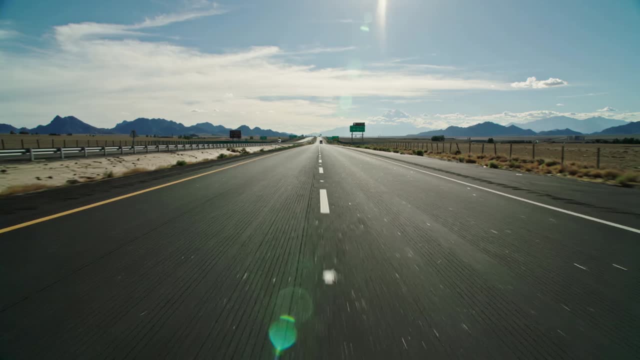 Moving cam filming forward as vehicle driving along desert road showing dashed centerline and sign