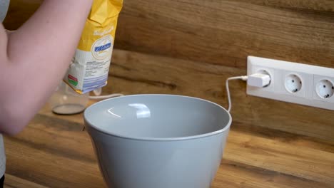 woman adding a spoon of flour to a bowl