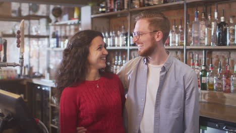 retrato de una pareja sonriente propietaria de una barra de pie detrás del mostrador