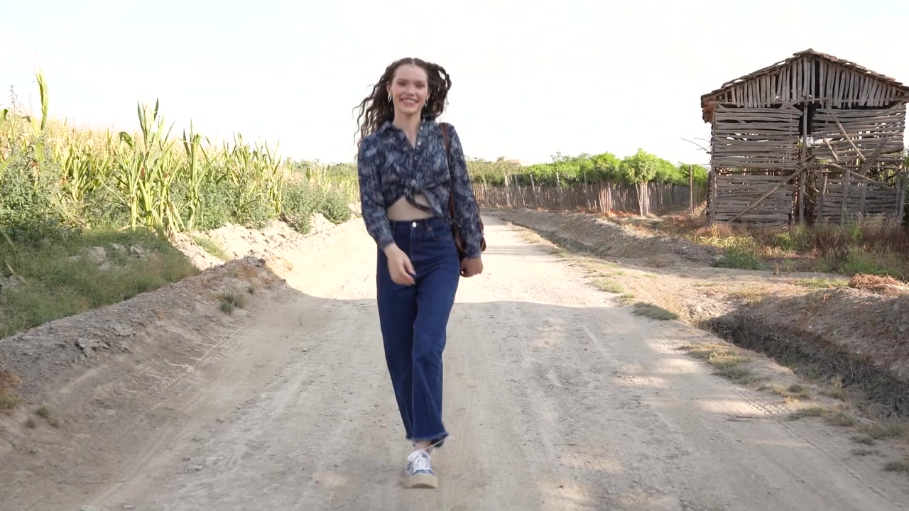 Una mujer joven paseando tranquilamente por un camino polvoriento rodeada de un pintoresco viñedo.