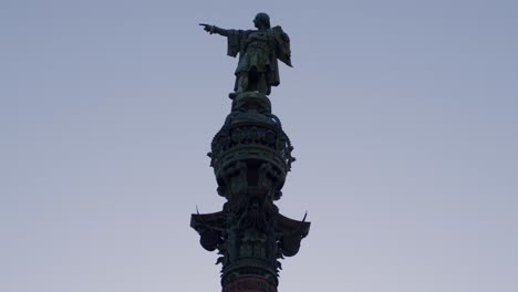 silhouetted christopher columbus statue pointing towards the sea at twilight in barcelona