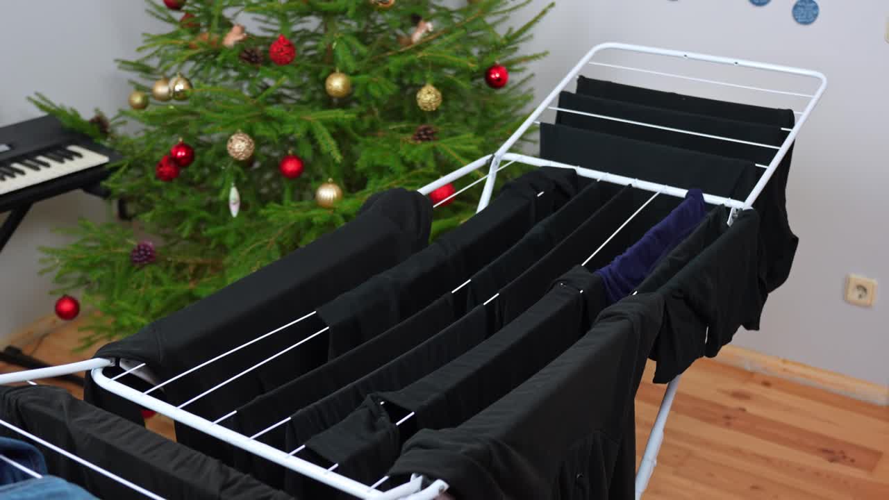 Indoor clothes drying rack with jeans and dark laundry on a wooden floor, Christmas tree and decorations softly visible in the cozy family room background