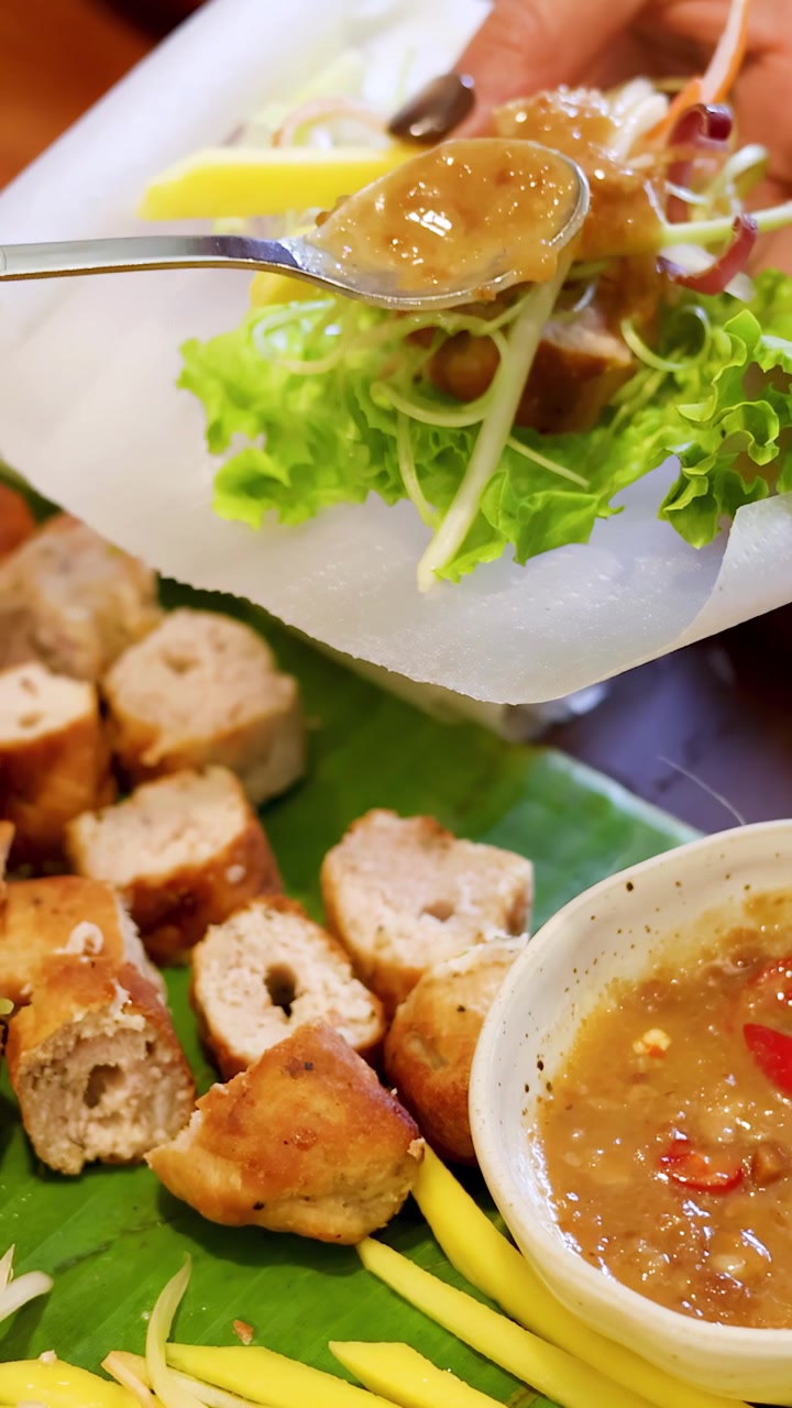 ภาพโคลสอัพมือที่กำลังทำปอเปี๊ยะเวียดนามสดไส้หมูย่างพร้อมน้ำจิ้มถั่ว