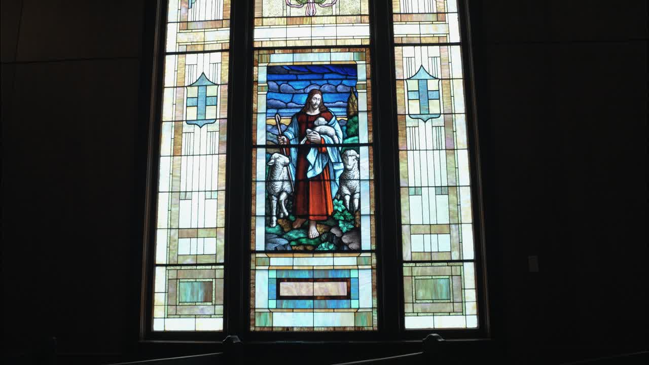 Stained-glass church window depicting Jesus as the Good Shepherd with sheep, symbolizing faith, guidance, and Christian spirituality in a sacred space