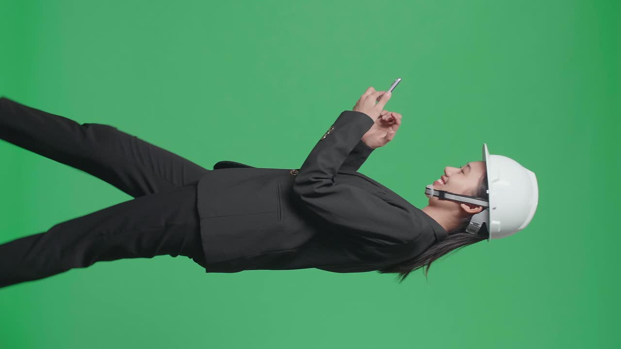 Side View Of Smiling Asian Female Engineer Using Smartphone And Walking In The Green Screen Studio