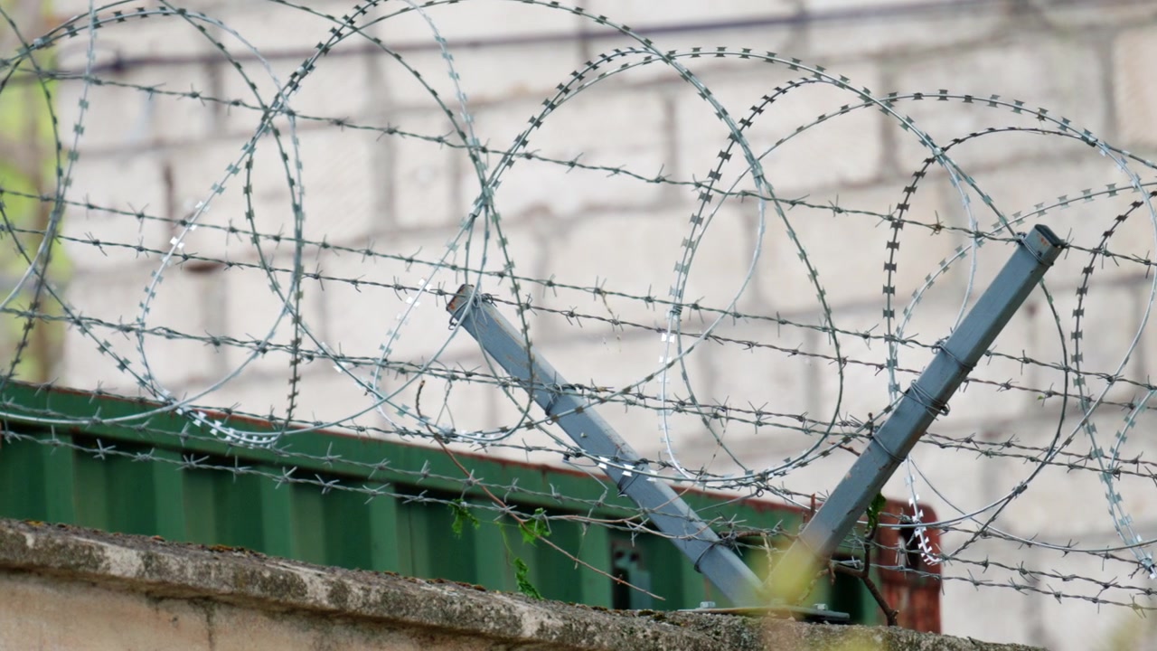 A sharp close up of barbed wire stretched across a fence, with a blurred building in the background