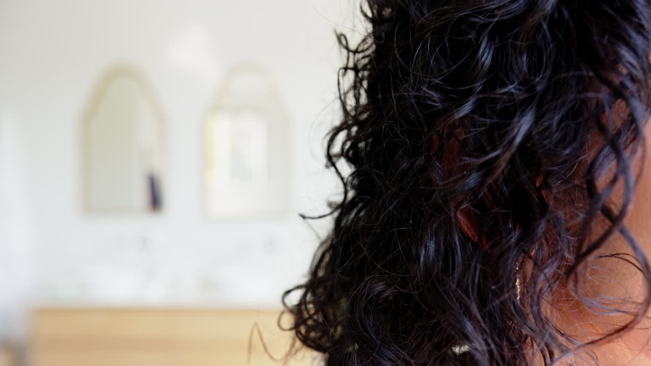 Close-up of asian woman with curly hair and hoop earring in modern bathroom, at home, copy space