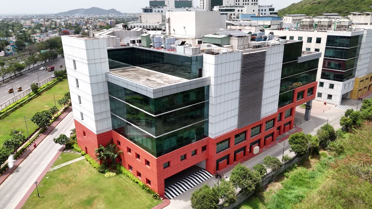 Aerial shot of a modern urban tech park with a green backdrop, a multi-storey corporate campus located next to a busy highway and a dense, green hillside. accents and visible rooftop solar panels