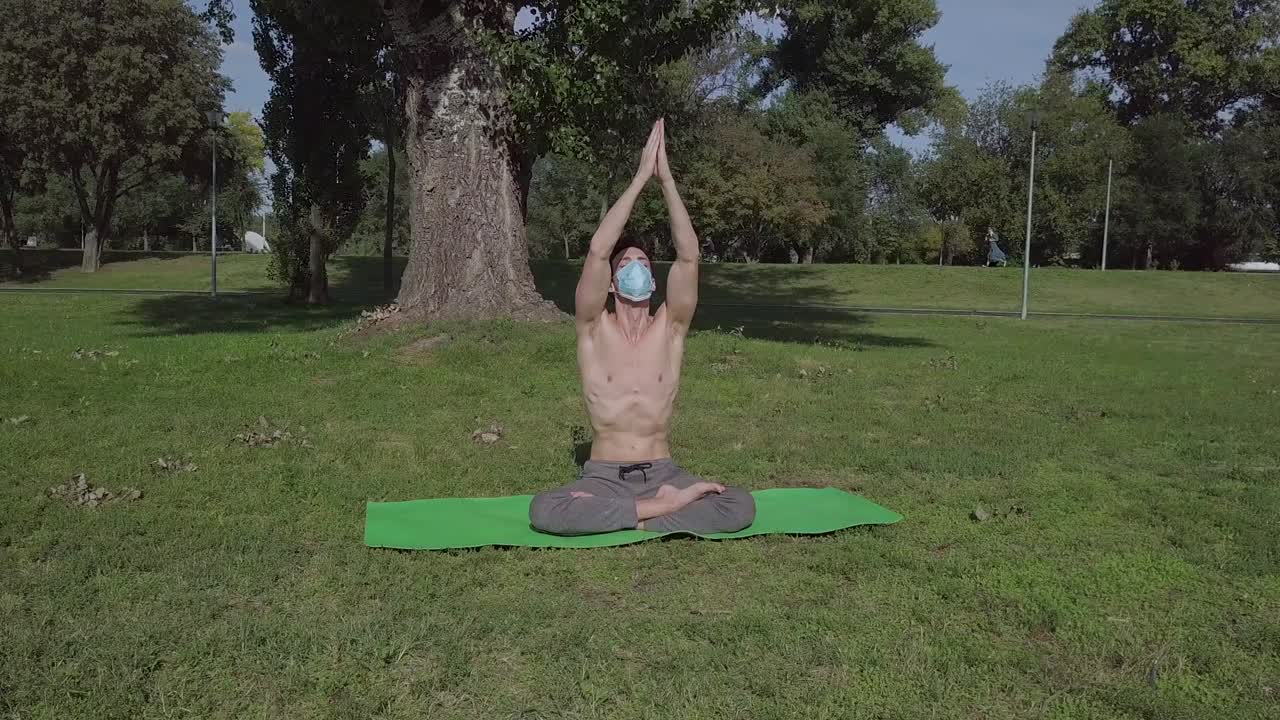 Lindo jovem com máscara fazendo alongamento de ioga no parque durante a epidemia de COVID, estilo de vida natural.